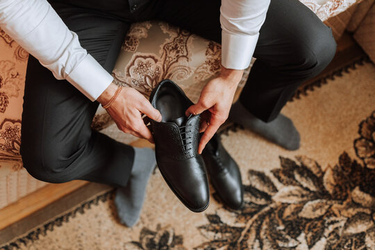 An elegant man wears black leather formal shoes. Tying shoes. Business man tying shoelaces on the floor. Up close The groom is preparing for the wedding.