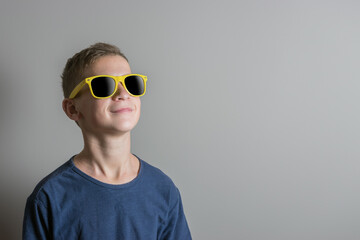 Teenager boy in sunglasses and blue t-shirt on bright background.