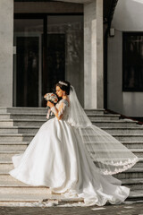Obraz premium Beautiful bride with a wedding bouquet of flowers, attractive woman in a wedding dress with a long veil. Happy bride woman. Bride with wedding makeup and hairdo. Winter wedding