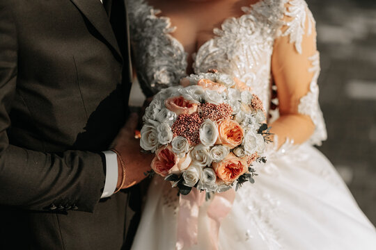 The bride is holding a beautiful wedding bouquet of pink flowers. White wedding dress with beaded sleeves