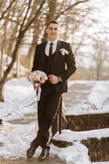 portrait of a handsome and manly groom in a black suit with a tie. Groom in nature in the winter...