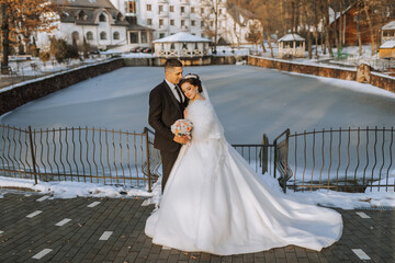 Obraz premium Winter wedding. Happy couple walking in wedding clothes hugging and smiling in a winter park covered with snow on their wedding day. Winter love story of a beautiful couple in snowy winter weather