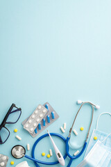 Clinic essentials. Vertical top view of stethoscope, face masks, pill packs, thermometer, and glasses on a serene pastel blue background. Space for text or promotion