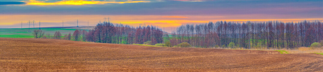As the fiery sun sets behind the horizon, a plowed field stands illuminated by the warm embrace of...