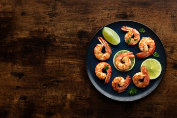 Shrimps, shot from above with a place for text on a wooden table. Cooked shrimp with lime, tasty gourmet dish - obrazy, fototapety, plakaty