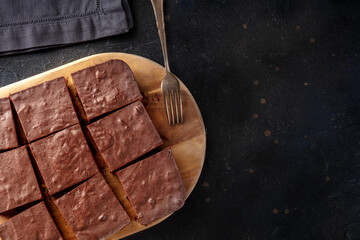 Chocolate brownie, simple coffee cake, overhead flat lay view on a black slate background with copy space