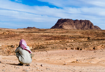 Bedouin in white red scarf in the desert against the backdrop of mountains and blue sky in Egypt...