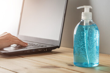 Hand sanitizer in a bottle on wooden table with a laptop. Coronavirus prevention concept.