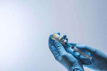 Hands in blue latex gloves fill in syringe with vaccine from glass vial. Vaccination and medical...