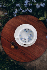 in the garden, among the small flowers, there is a white tea cup on a beautiful round wooden stand