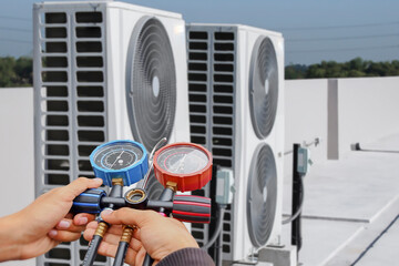 Air conditioning, HVAC service technician using gauges to check refrigerant and add refrigerant.	