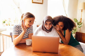 Three pretty female teenagers of different nationalities are looking at the laptop screen and...