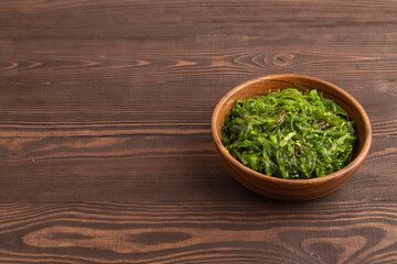 Chuka seaweed salad in wooden bowl on brown wooden. Side view, copy space.