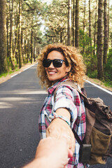 Happy travel couple woman holding man hands with outdoor nature woods around - people following and enjoying vacation together - healthy lifestyle and backpack trip adventure in the forest