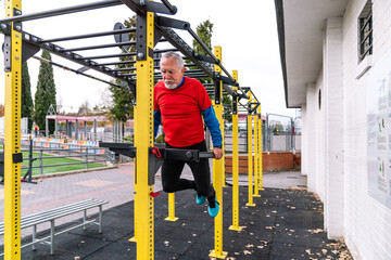 Senior man in red shirt engages in leg lift exercise on yellow outdoor gym equipment, maintaining...
