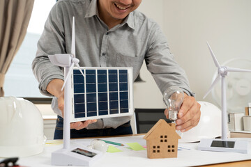 Businessman holding solar panels and light bulbs at the office.