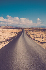 Fototapeta na wymiar Long straight asphalt road with sand and rocks desert around - travel and destination adventure concept - beautiful landscape and blue sky with clouds in background