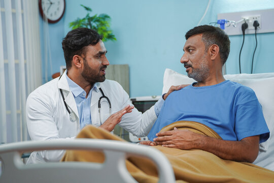 Indian doctor consoling sick elderly patient at hospital ward during routine visit - concept of medical treatment, building confidence and motivation
