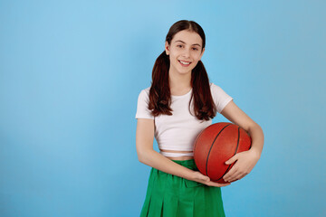 Young brunette teenage girl with basket ball and ponytails on blue background.