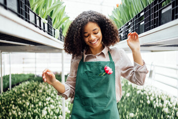 Smiling attractive darkskinned female gardener with flower on her workplace