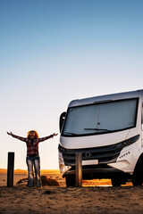 Woman standing outstretching arms and enjoying freedom and travel lifestyle with modern camper van....