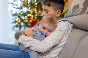Happy family,Preteen child, boy brother, hugging his little newborn sibling at home, sitting on the...