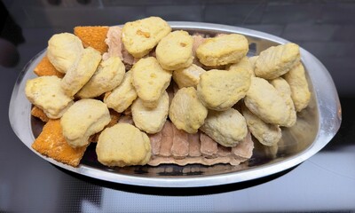 Unprepared and frozen fast-food snacks on a plate before deep frying including chicken nuggets and cheese snacks with bread crums