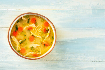 Chicken noodle soup with vegetables, a bowl of healthy stock, top down shot on a rustic wooden...