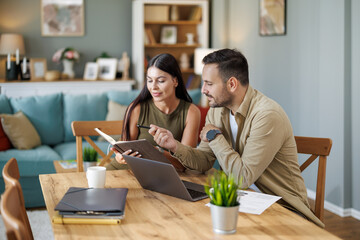 Married couple sit at a table in the living room with laptop,working from home office