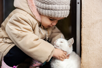 A cute little girl is playing with a domestic cat.