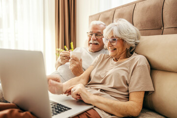 A happy senior couple using laptop in bed in the morning. - Powered by Adobe