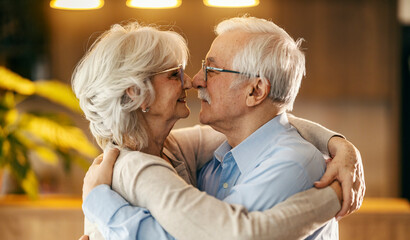 An affectionate senior couple hugging and standing face to face.