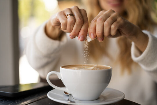 Close-up of female hands pours sugar into coffee. Adding sweetener or fructose to beverage. Daily drink, unhealthy food