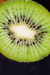 Macro shot of cut green kiwi, selective focus, black background, vertical, with copy space