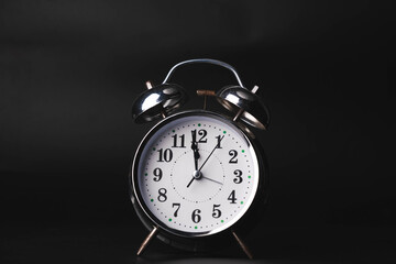 Close-up of a retro alarm clock face on a black background. Clock hands move fast, the beginning of...