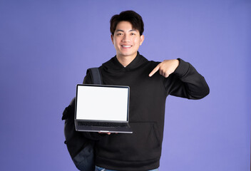 Asian male student using laptop on purple background