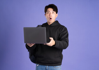 Asian male student using laptop on purple background