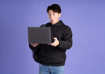 Asian male student using laptop on purple background