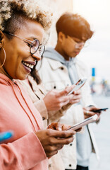 Vertical photo. Addicted diverse young people using mobile phone outdoors Millennial friends having fun while watching social media video content on cell phone app. Youth and technology concept