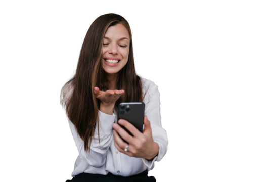 Cheerful Hispanic young woman holds phone sends air kiss during video call against transparent background dressed in shirt. brunette businesswoman grateful to her husband. Happy woman