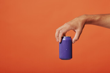 cropped view of person holding purple soda can in hand on orange background, carbonated drink - obrazy, fototapety, plakaty