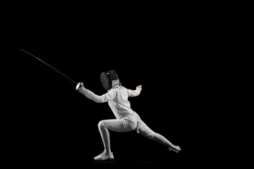 Fencer's footwork and poised stance in mid-bout against pristine black studio background. Tactical aspect dynamic sport. Concept of professional sport, active and healthy lifestyle, championship. Ad