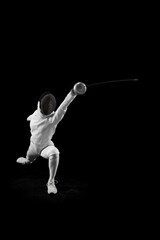 Female fencer glides across floor, her blade in motion against black studio background. Sportsman...