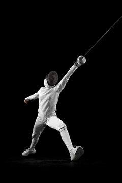 Dynamic portrait of female fencer lunges forward, her blade poised to strike, she closing in fast against black studio background. Concept of professional sport, active lifestyle, championship. Ad