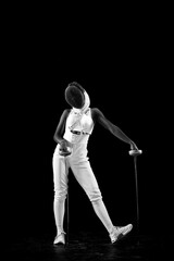 Fototapeta na wymiar Fencing maestro, delicately leaning on fencing foil, radiating confidence and poise against black studio background. Blend of strength and grace. Concept of professional sport, championship. Ad