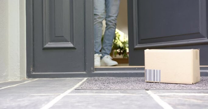 Low section of biracial man picking up cardboard box outside front door, copy space, slow motion