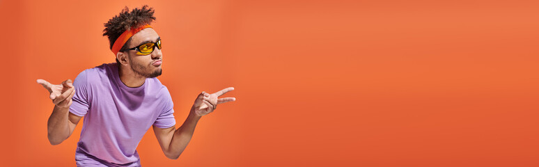 african american man in eyeglasses pouting lips and gesturing on orange background, banner