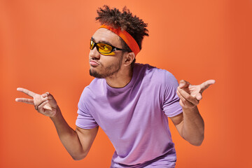 african american man in eyeglasses and headband pouting lips and gesturing on orange background