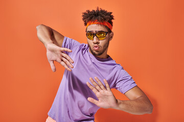 expressive african american man in eyeglasses and headband gesturing on orange background