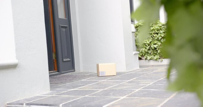 Biracial man picking up delivery in cardboard box outside front door, copy space, slow motion